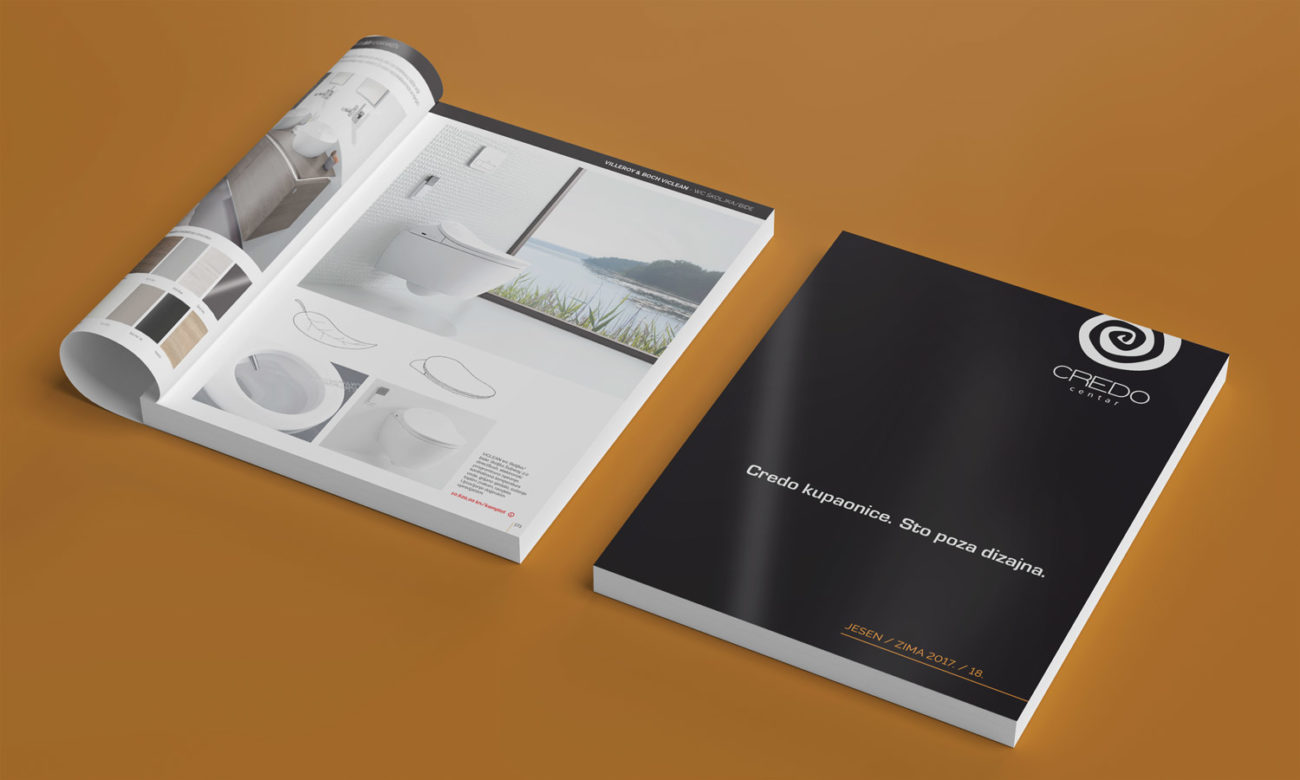Na slici je prikazan Credo Centar katalog na jarko narančastoj podlozi. Jedan katalohg je zatvoren pa vidimo crno bijelu naslovnicu, a drugi je otvoren pa vidimo sliku kupaonice.