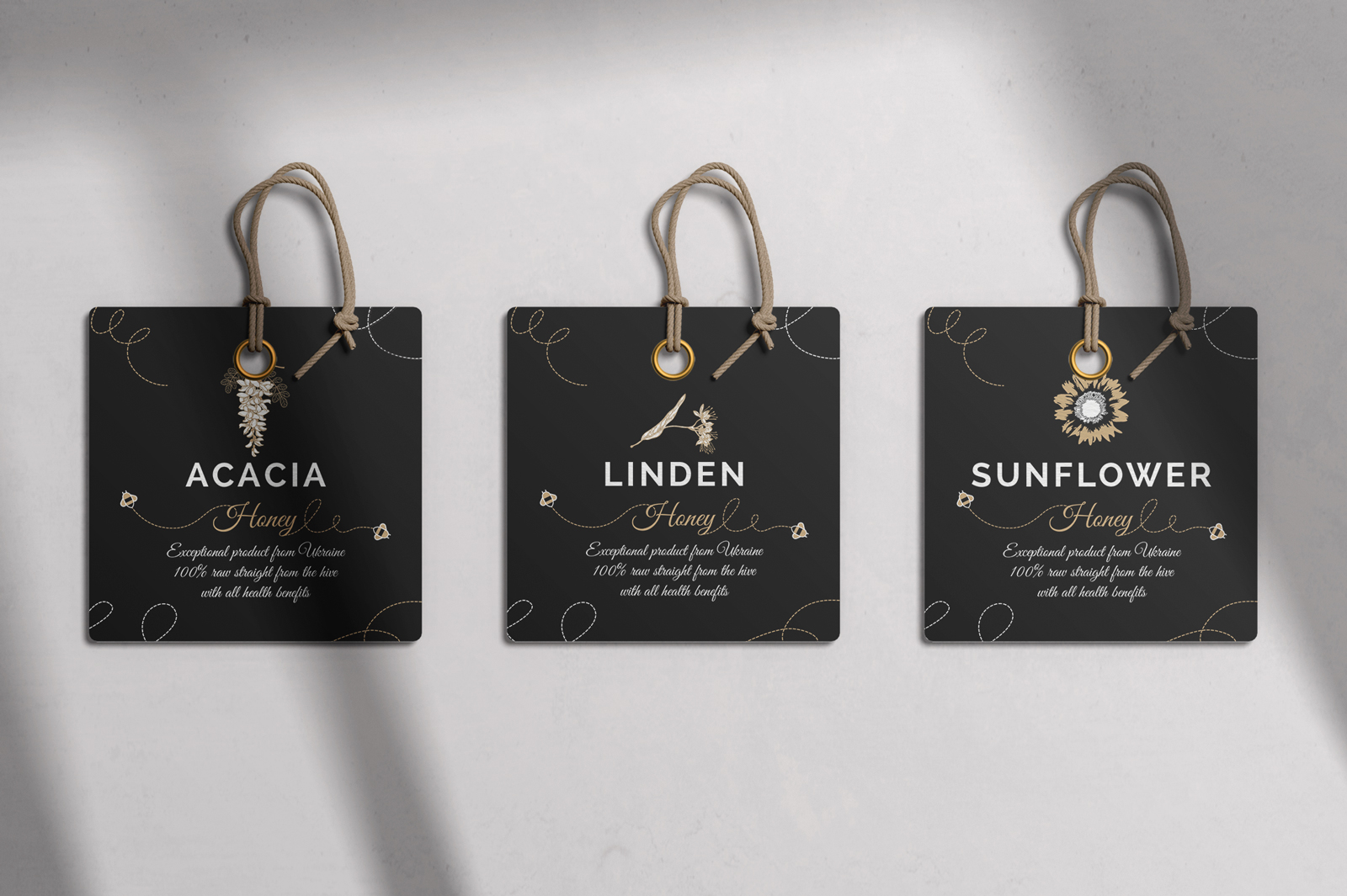 Dizajn etikete za med Shevchenko. Na slici su tri etikete položene na bijelu podlogu. Na podlozi vidimo sjene prozora. Etikete su crne boje sa zlatnim i bijelim ikonama i slovima.